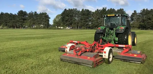 John Deere tractor with a Trimax triple mower cutting a large striped field