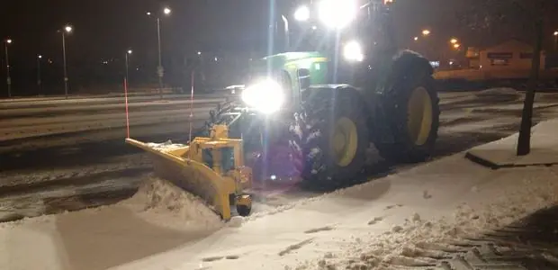 Tractor and snow plough clearing a car park at night